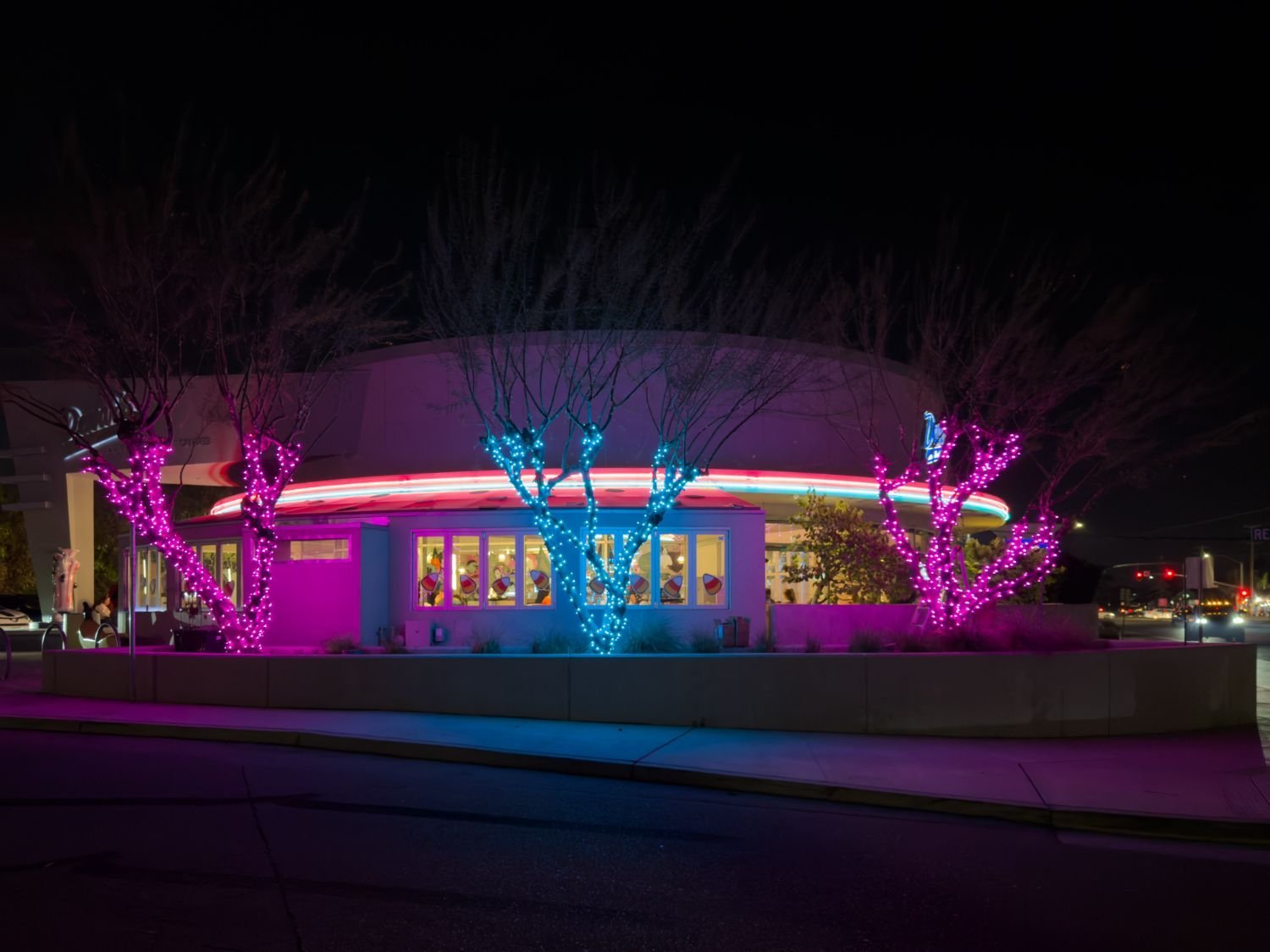 The Light Guys holiday installation at Dewar’s Ice Cream, with pink and blue lights wrapping trees outside the storefront